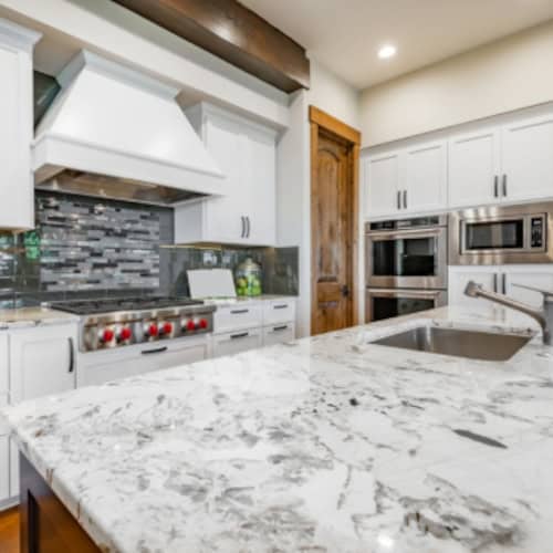 Modern kitchen with white cabinets and marble countertop in Fika community.